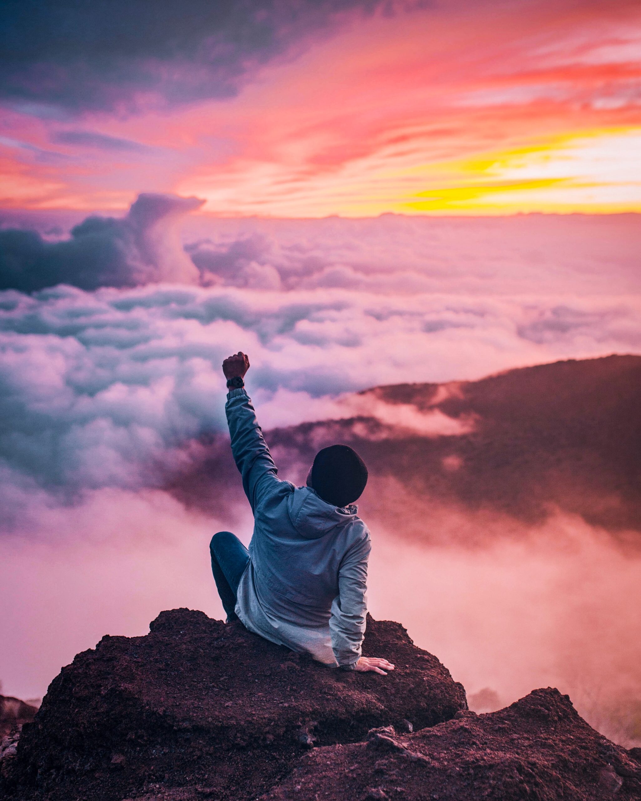Person throwing up their fist on top of a mountain at sunset